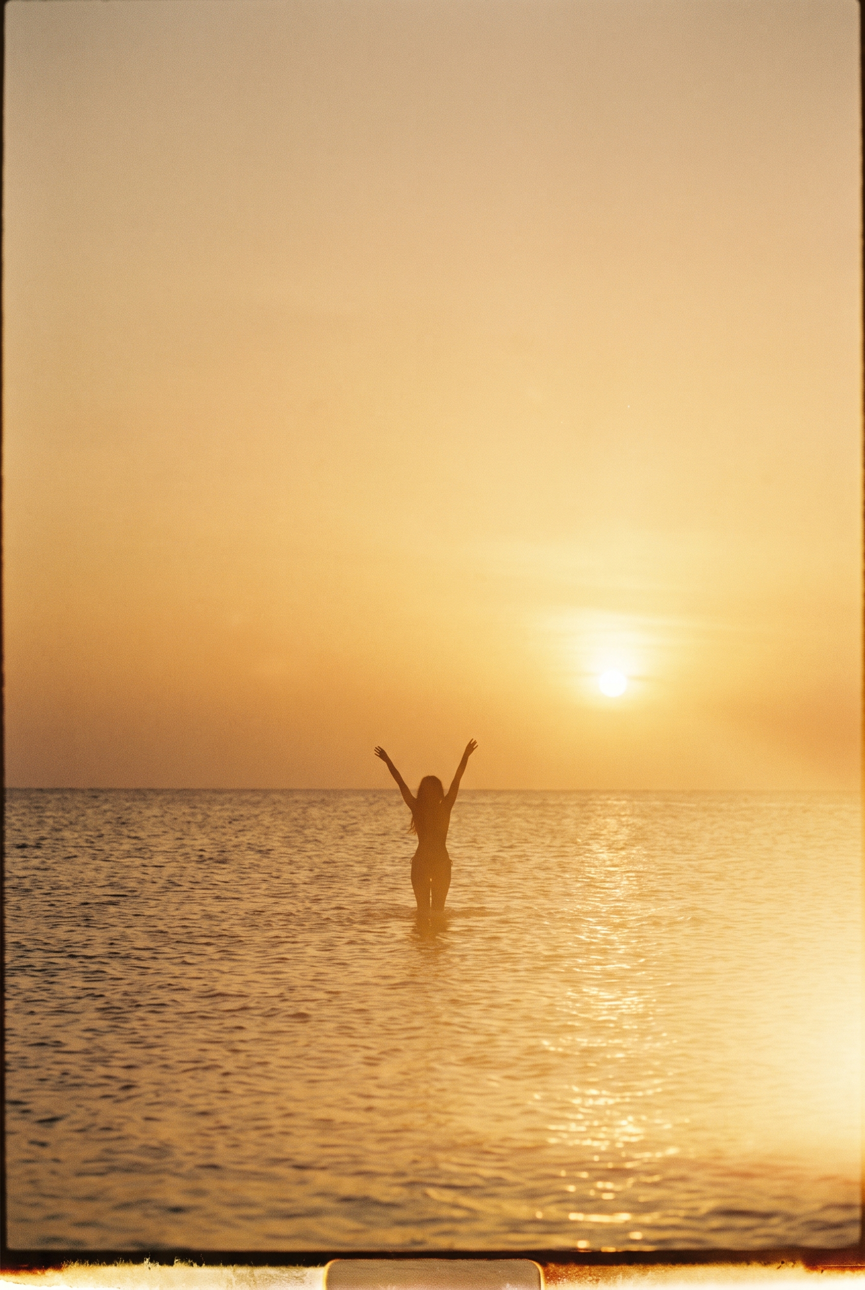 Distant backlit silhouette of a woman standing in shallow water at sunset
